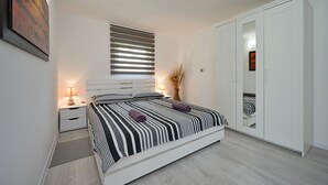Une chambre à coucher comprenant un lit, des tables de chevet, une fenêtre avec des stores, une armoire et un miroir.