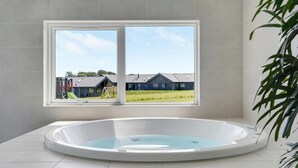 Een moderne badkamer met een groot bad, een raam met uitzicht op een woonwijk, en een kamerplant.