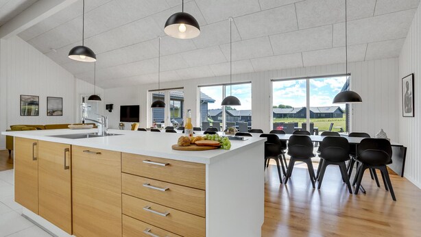 Een moderne keuken met een groot eiland, houten kastjes en zwarte hanglampen.