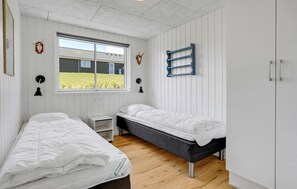 Ein Zimmer mit zwei Einzelbetten, einem Fenster mit Blick auf ein Haus, einem Wandregal und einem kleinen Nachttisch.