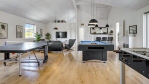 Een ruime kamer met een tafeltennistafel, een poolbiljart en een biljart, met houten vloeren en witte muren.