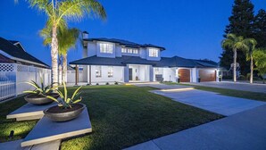 A modern two-story house with a well-maintained lawn, a driveway, and a white fence.