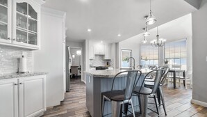 A modern kitchen with white cabinetry, a granite countertop, and a central island with bar stools.