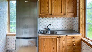 Uma cozinha compacta com armários de madeira, geladeira de aço inoxidável, pia e janela com vista para o verde.