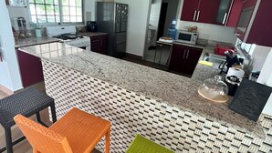 Una cocina moderna con encimera de granito, dos sillas de mimbre, un refrigerador y un microondas.