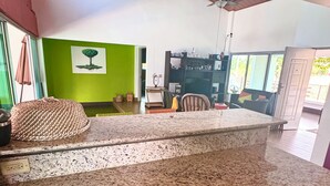 Una cocina con encimeras de granito, un armario rojo y una pared verde con un cuadro de un árbol.