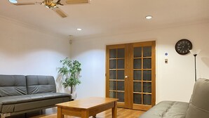 A living room with a sofa, a coffee table, a plant, a wooden door with glass panels, and a ceiling fan. - Hawker 4BR House（Air-Con, WiFi, Netflix, Parking） (Hawker)