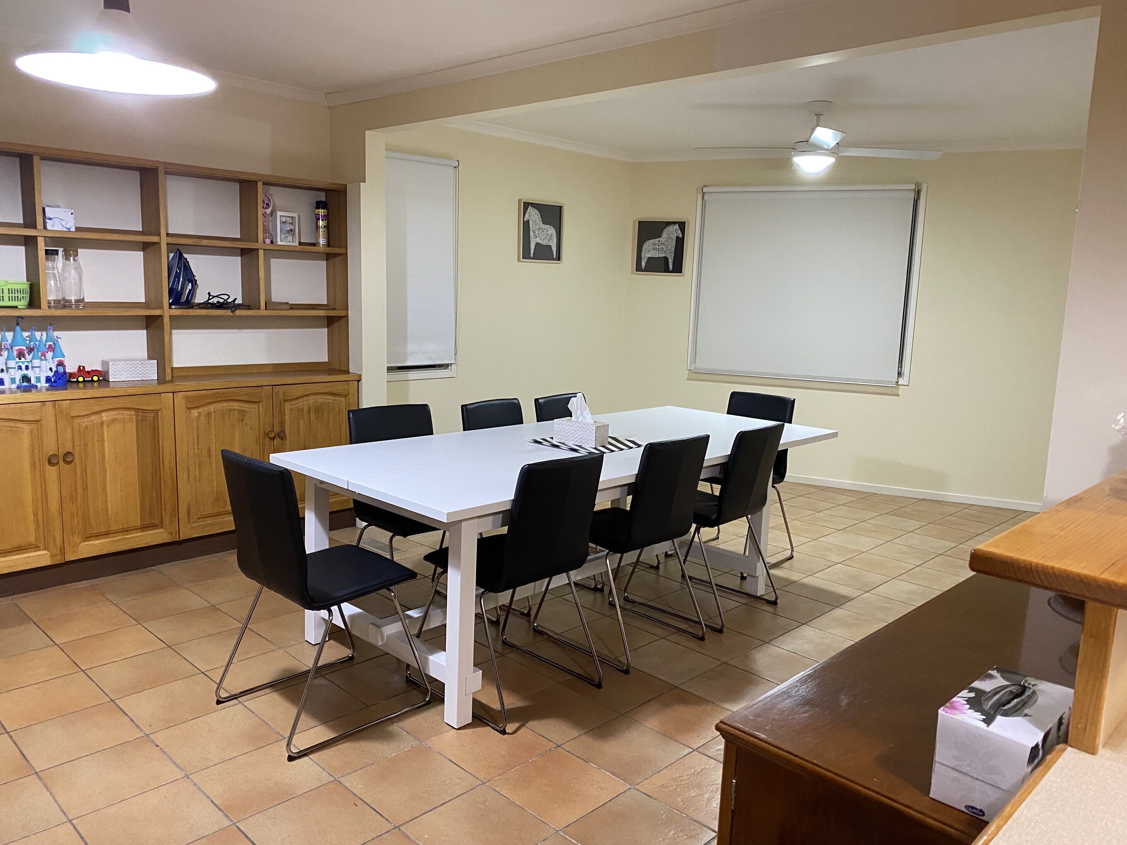 A conference room with a white table, black chairs, a wooden cabinet with shelves, and a projector screen.