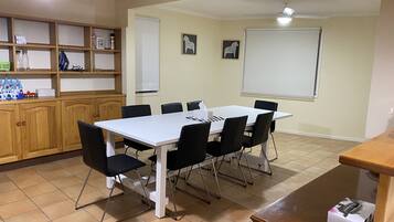 A conference room with a white table, black chairs, a wooden cabinet with shelves, and a projector screen.