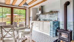 A modern kitchen with a wood-burning stove, white cabinets, and a large window overlooking a garden.