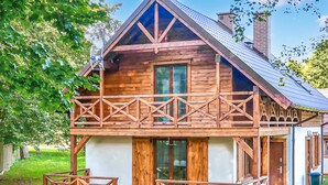 A wooden cabin with a balcony, large windows, and a chimney.