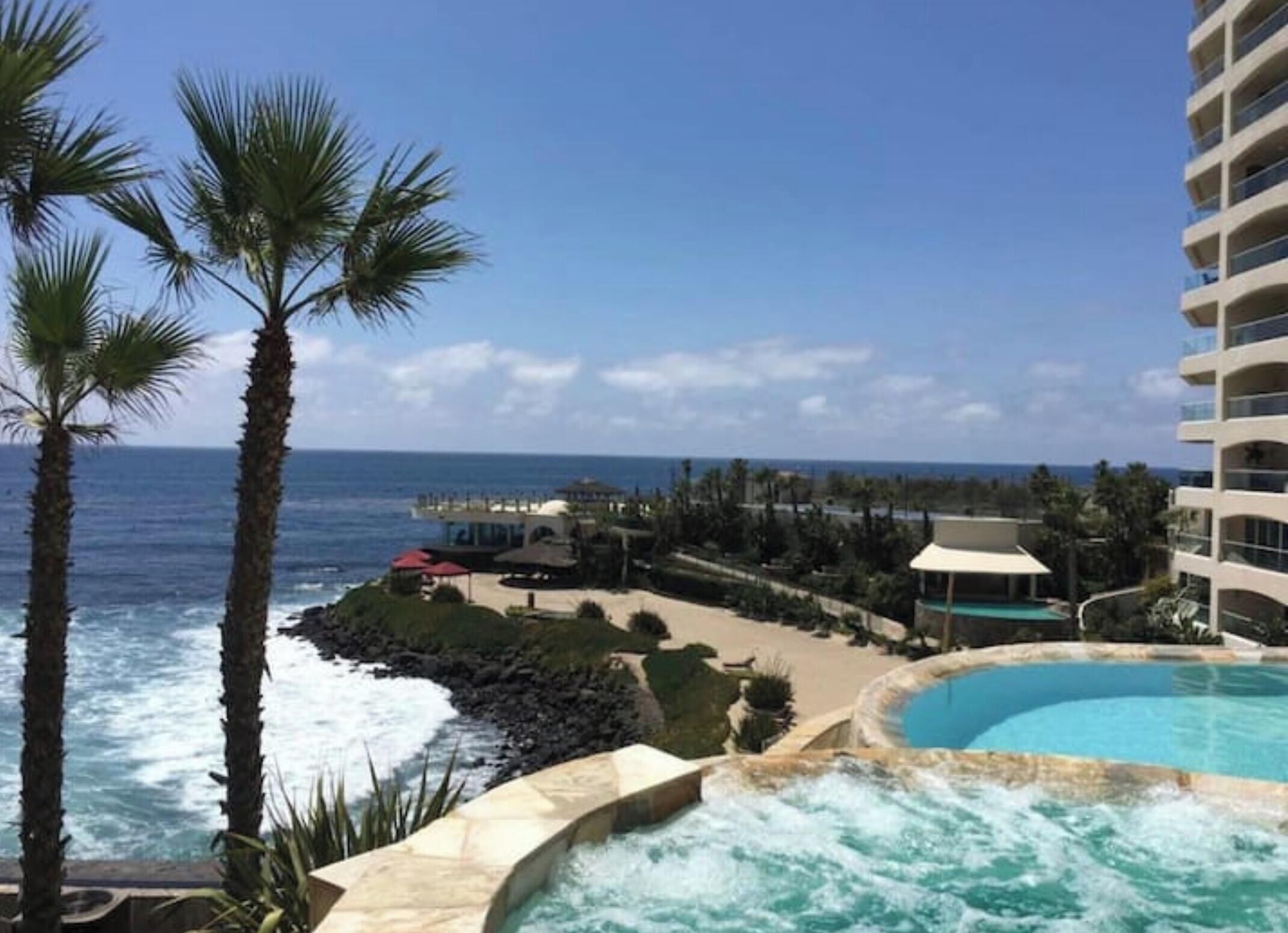 A resort with a pool, ocean view, and palm trees.