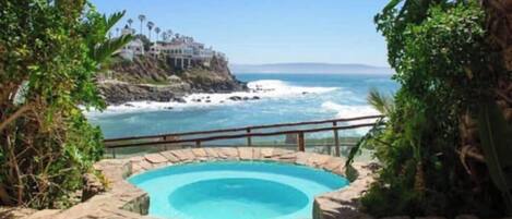 A stone pool with a view of the ocean and a cliffside building.