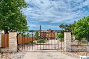 A gated property with a metal gate, a stone wall, and a house in the background.