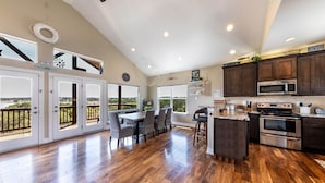 A spacious kitchen with wooden flooring, a dining area with chairs, a large island, and a view through the doors.