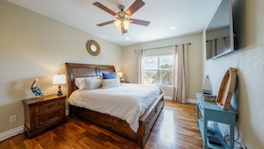 A bedroom with a wooden bed, nightstands, a ceiling fan, a window with curtains, and a mounted TV.