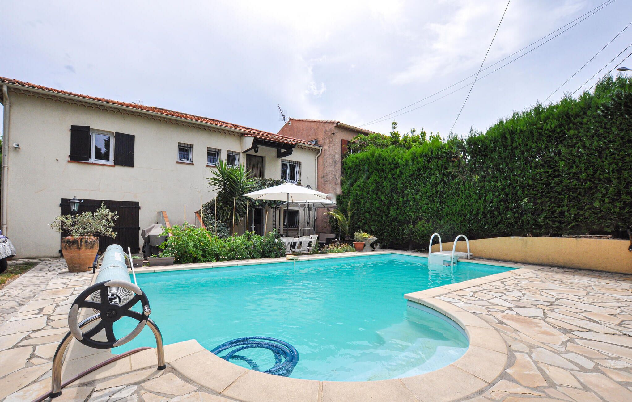 Ein Schwimmbad mit einer Steindeck, eine Lounge-Ecke mit Tisch und Stühlen sowie eine hohe Hecke.