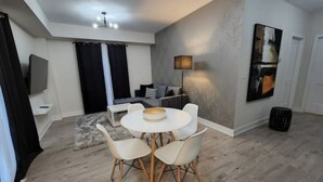 Una sala de estar moderna con comedor, que incluye una mesa redonda con sillas, un sofá, un televisor de pantalla plana y un cuadro en la pared.