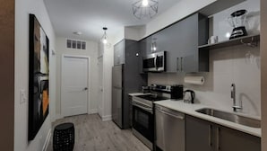 Una cocina moderna con electrodomésticos de acero inoxidable, una encimera blanca y una lámpara colgante.