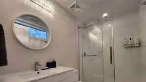 Un baño moderno con un espejo redondo, un lavamanos blanco, un inodoro y una ducha con mampara de vidrio.