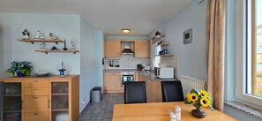 A compact kitchen with wooden cabinets, a dining table with chairs, and a window with curtains. - Apartment i1 - 2-room apartment on the 1st floor for 3 persons, approx. 50 m² with WLAN (Graal-Müritz)