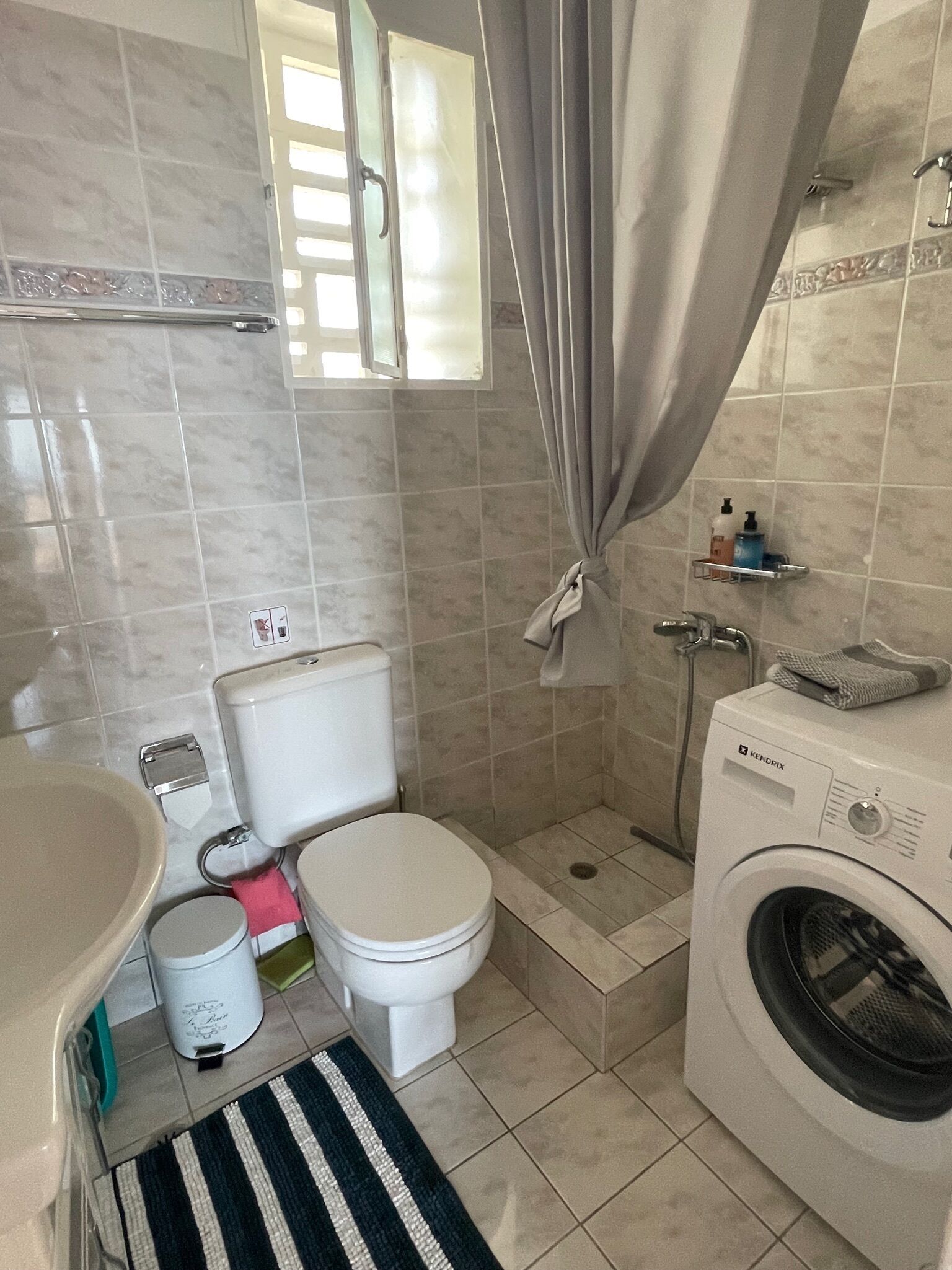 A bathroom with a toilet, washing machine, and a shower area.
