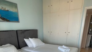 Een hotelkamer met twee bedden, een grijs hoofdeinde, een grote kledingkast en een schilderij aan de muur.