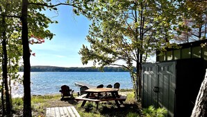 A wooden deck leading to a picnic table with chairs, overlooking a lake. - Big Twin Lodge-Fall Color Haven! Off-Roading, Snowmobiling, Wooded Seclusion! (Mancelona)