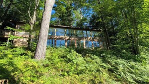 A cabin with a wooden deck, surrounded by dense forest. - Big Twin Lodge-Fall Color Haven! Off-Roading, Snowmobiling, Wooded Seclusion! (Mancelona)