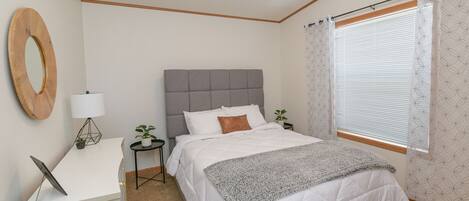 A bedroom with a bed, bedside tables, a desk, a lamp, and a window with curtains.