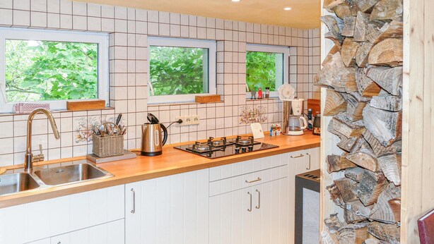 A modern kitchen with white cabinets, a stainless steel sink, and a gas stove. There are three windows providing natural light, and a stone wall on the right side. - Gorgeous home in Tharandt with WiFi (Tharandt)