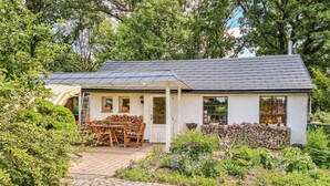 A small, white cottage with a tiled roof, a wooden table and chairs outside, and a garden with various plants and flowers. - Gorgeous home in Tharandt with WiFi (Tharandt)