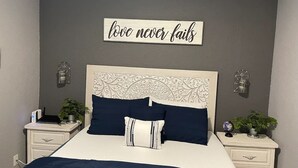 Une chambre à coucher comprenant un lit, deux tables de chevet, un panneau mural et deux appliques murales.