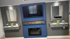 Un salon moderne doté d’une cheminée intégrée, de deux téléviseurs fixés au mur et d’étagères décoratives.