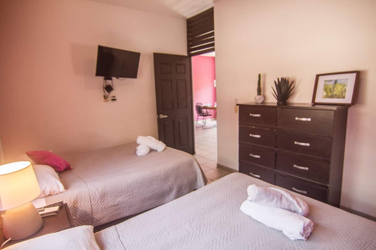 A hotel room with two beds, a TV mounted on the wall, a dresser, and a door leading to another room.