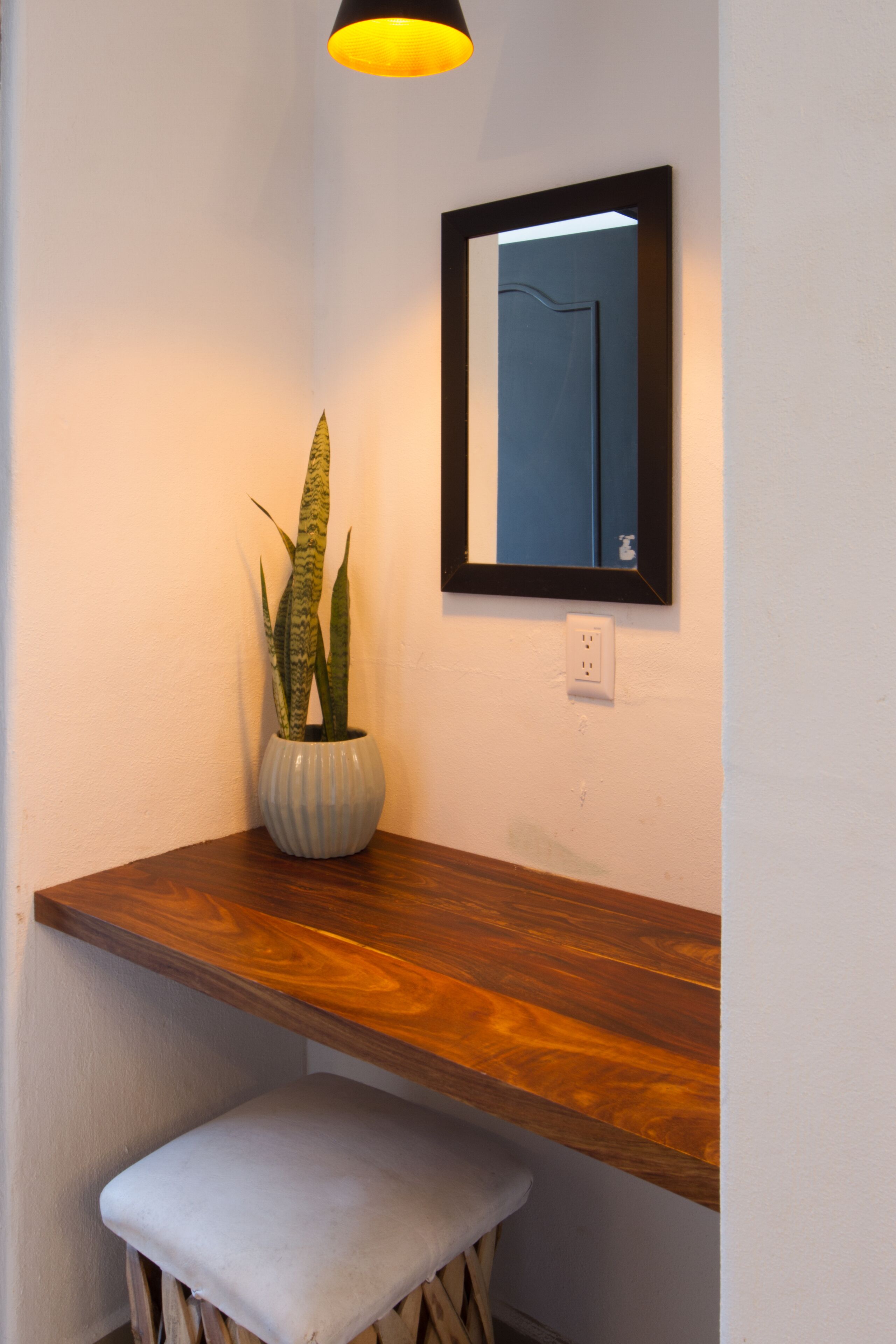 Un coin avec un banc en bois, une plante en pot, un miroir et une prise électrique.