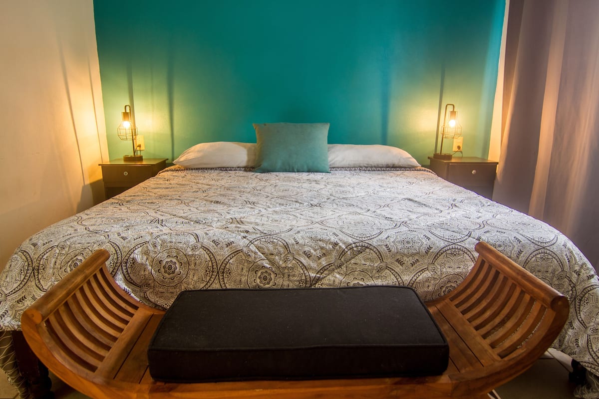 A neatly made bed with a patterned bedspread, two bedside lamps, and a wooden bench in the center.