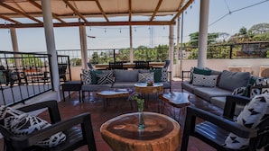 Un patio al aire libre con arreglos de asientos, incluyendo sofás y sillones, y una mesa de madera en el centro.