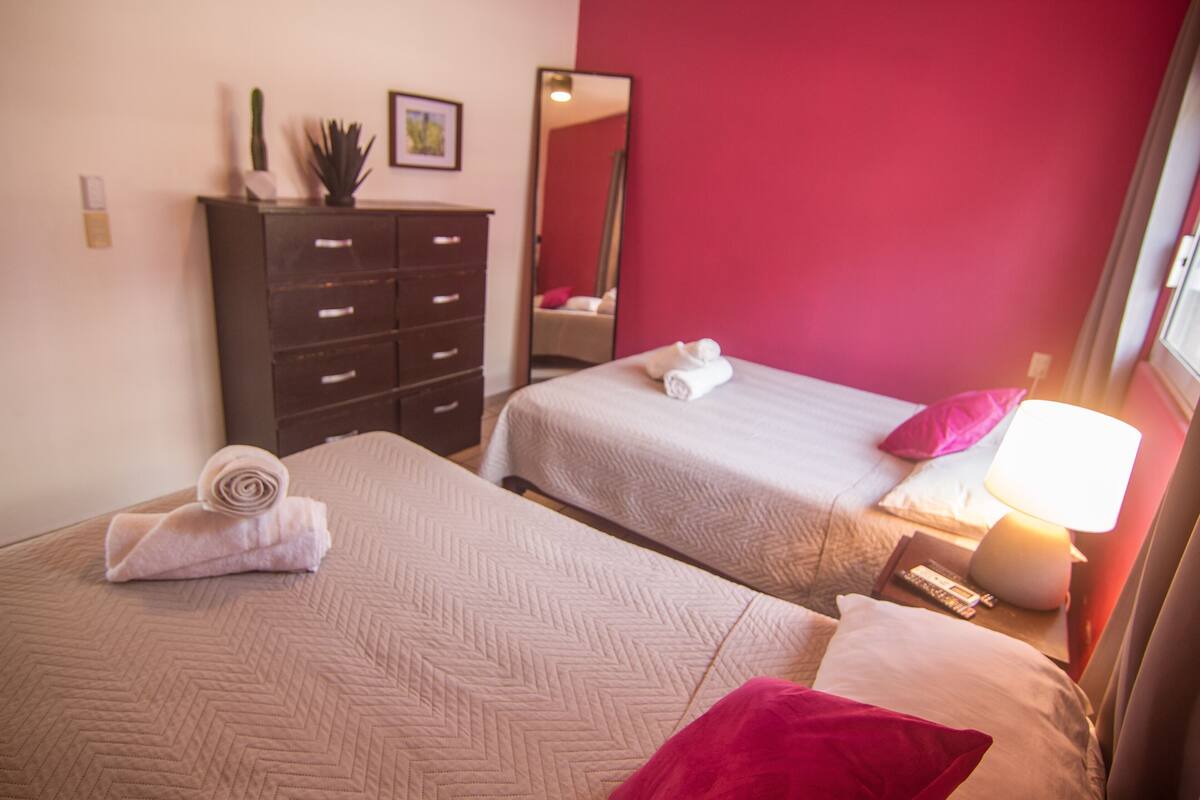 Two beds with rolled towels, a dresser, a mirror, and a nightstand with a lamp.