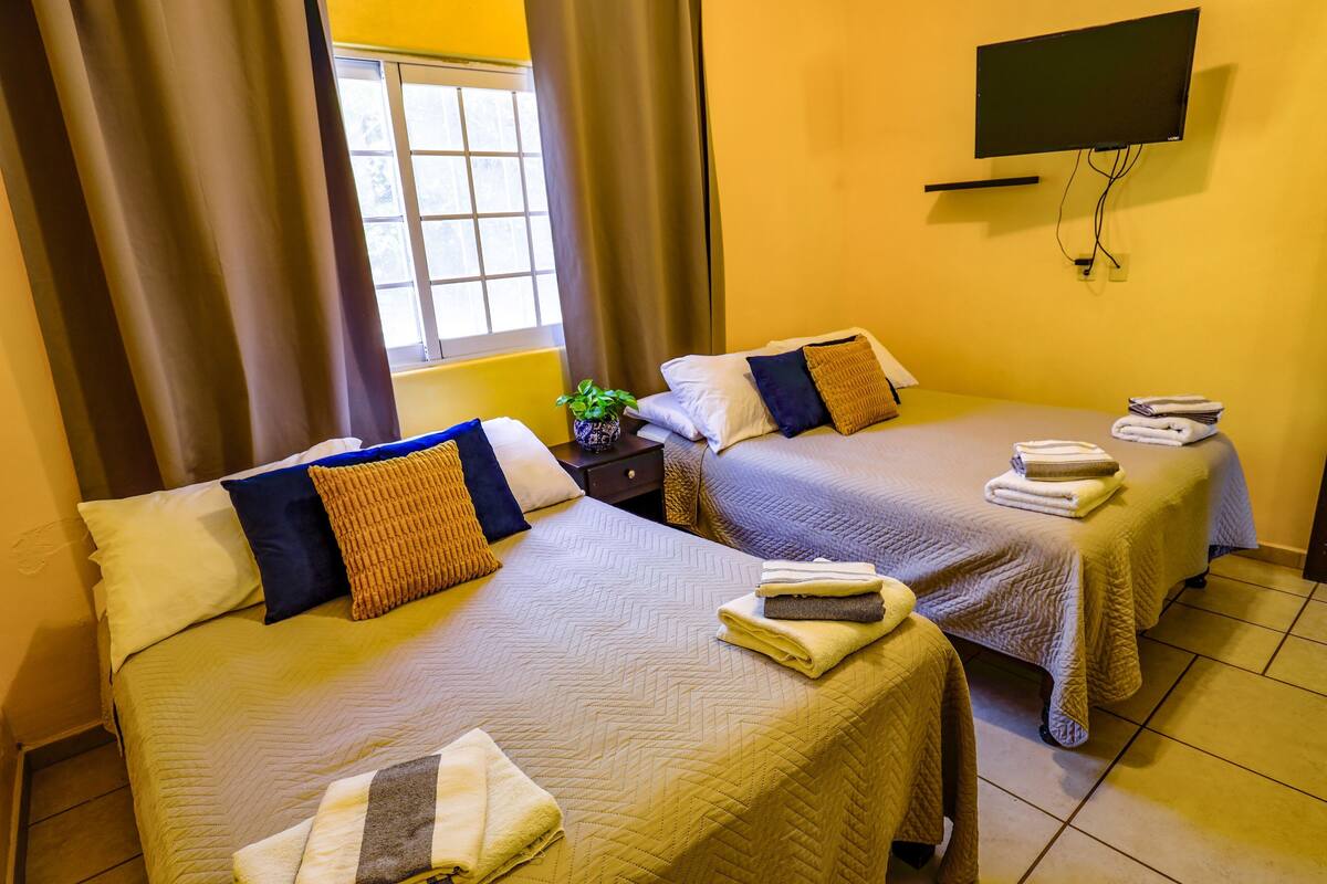 A hotel room with two beds, a TV mounted on the wall, and a window with curtains.