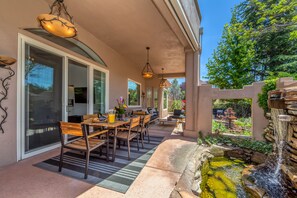 An outdoor patio with a dining table and chairs, a small waterfall feature, and a pergola with hanging lights.