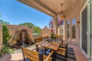 An outdoor patio with a stone water feature, wooden tables and chairs, and a view of the surrounding landscape.