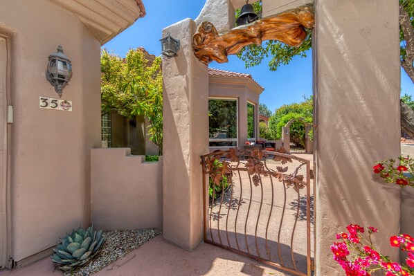 A gated entrance with a number sign, a wrought iron gate, and a stucco wall.