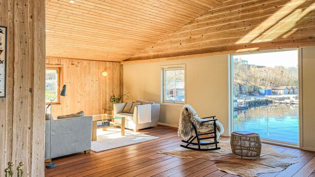 Un intérieur en bois avec un canapé, un fauteuil à bascule et une vue sur un plan d’eau à l’extérieur.
