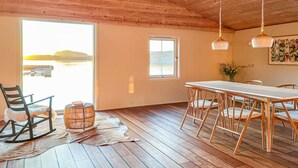 Une pièce spacieuse avec un plafond en bois, une grande fenêtre donnant sur l’eau, une table à manger avec des chaises et un luminaire suspendu.