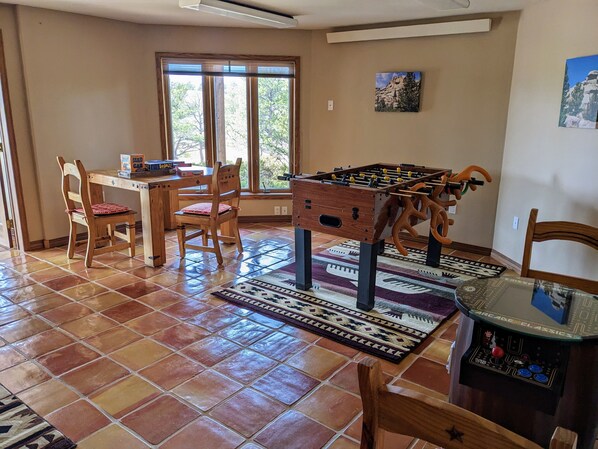 A room with a foosball table, a dining table with chairs, and a window with a view of trees. - Vedauwoo, Curt Gowdy State Park, Cheyenne, and Laramie close! (Cheyenne)