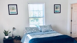 A bedroom with a bed, a nightstand, a potted plant, and two framed pictures on the wall.