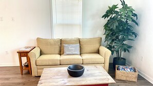 A living room with a beige sofa, a red coffee table, a small wooden side table, a potted plant, and a wicker basket.
