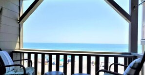 Een balkon met uitzicht op het strand, met twee stoelen en een tafel.