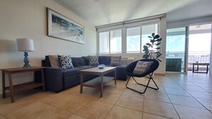 Un salon comprenant un canapé, une table basse, une lampe, un fauteuil et une grande fenêtre.